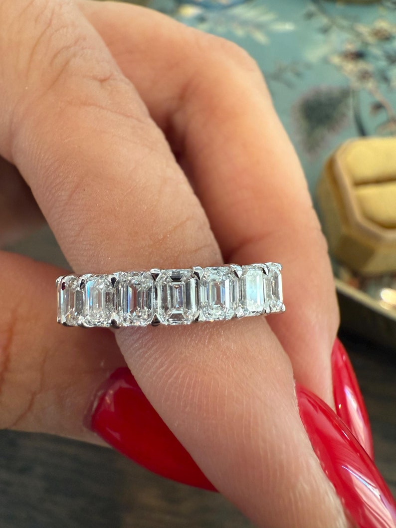 May include: A white gold eternity band featuring a row of emerald-cut diamonds.