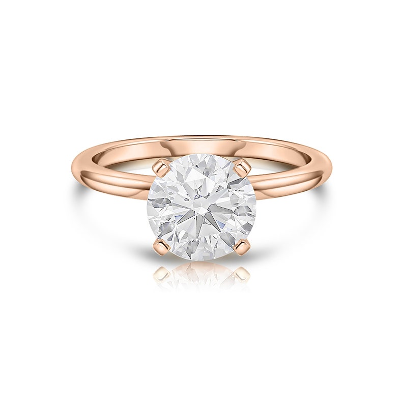 May include: A solitaire engagement ring with a round brilliant cut diamond set in a rose gold band.