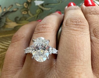 Könnte beinhalten: Ein großer ovaler Diamant-Verlobungsring mit kleineren birnenförmigen Diamanten auf beiden Seiten des Mittelstücks. Der Ring ist in einer Weißgoldfassung gefasst.