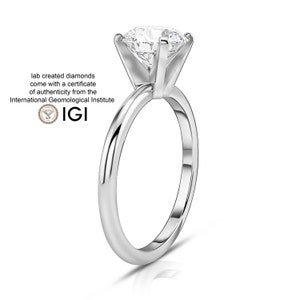 May include: A silver solitaire engagement ring with a round brilliant cut diamond. The ring is set in a simple band and has a polished finish.