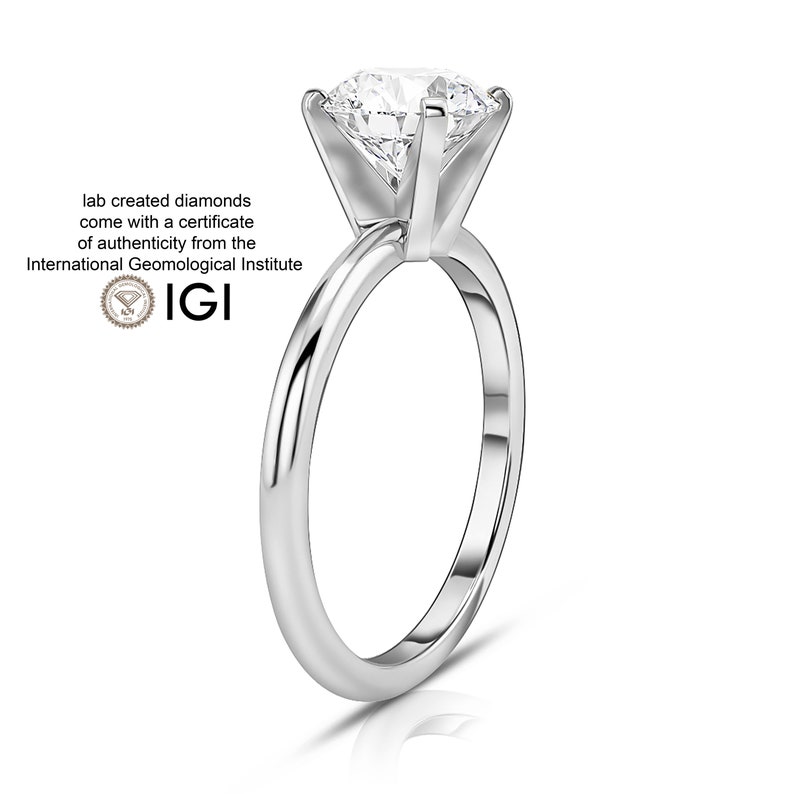 May include: A silver solitaire engagement ring with a round brilliant cut diamond. The ring is set in a simple band and has a polished finish.