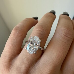 May include: A close-up of a silver ring featuring a large, oval-cut diamond. The diamond is the focal point, sparkling brightly against the silver band. The ring is set with prongs, and the design is simple and elegant.