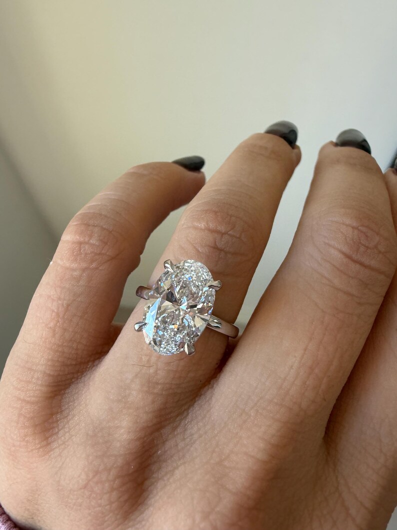 May include: A close-up of a silver ring featuring a large, oval-cut diamond. The diamond is the focal point, sparkling brightly against the silver band. The ring is set with prongs, and the design is simple and elegant.