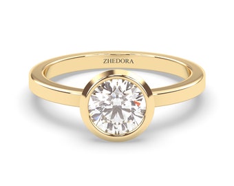 May include: A gold band ring with a bezel setting featuring a round, clear diamond. The ring is engraved with the word "ZHEDORA".