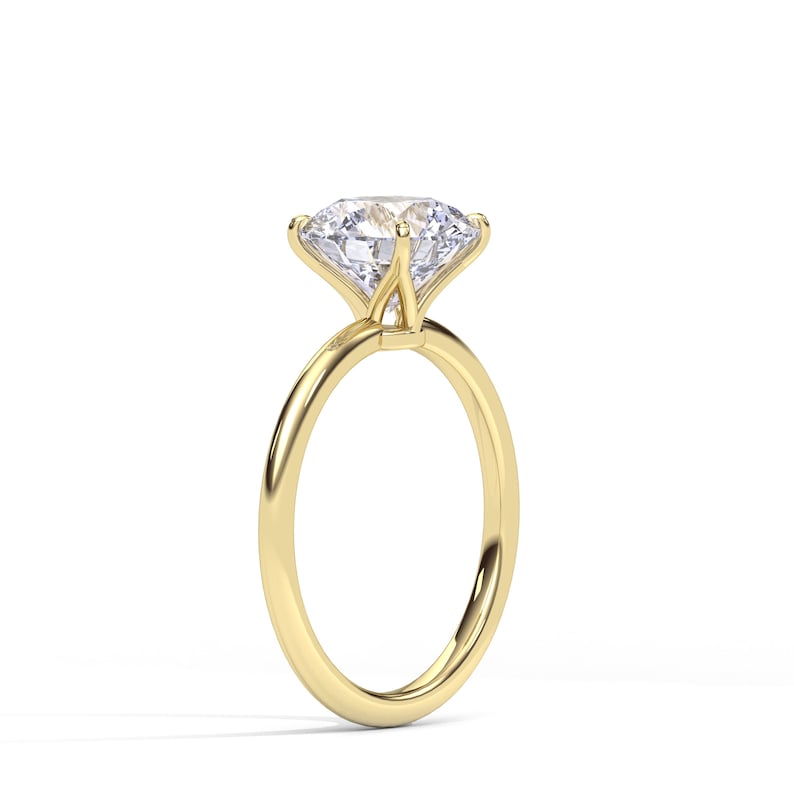 May include: A solitaire engagement ring with a large, clear, round-cut diamond set in a four-prong setting. The band is a polished gold color, and the ring is set against a white background.