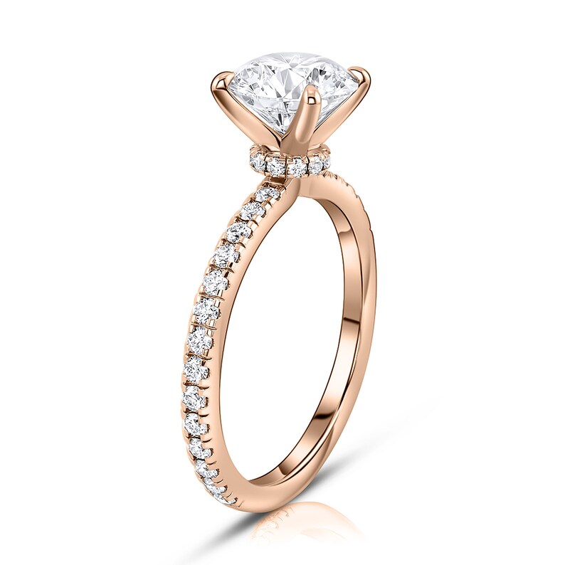 May include: A rose gold engagement ring with a round brilliant cut diamond center stone and a pave diamond band.