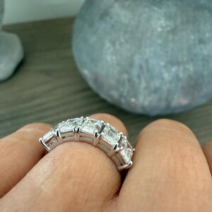 May include: A silver band ring with a row of emerald-cut diamonds set in a pave setting.