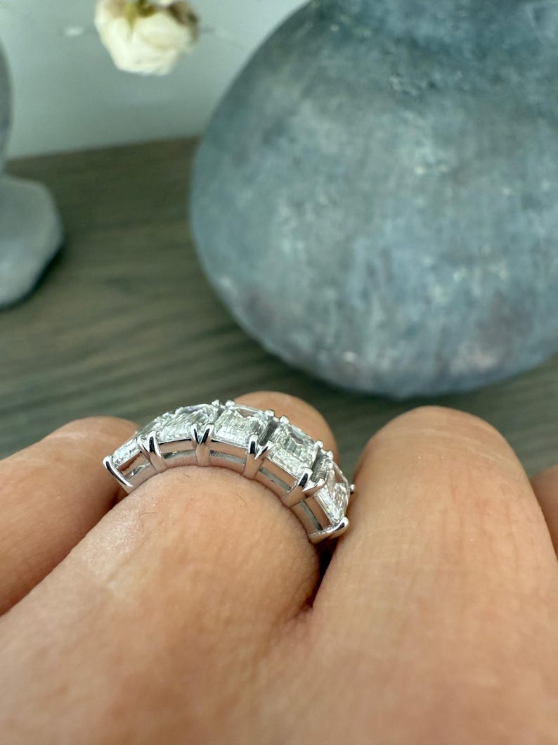 May include: A silver band ring with a row of emerald-cut diamonds set in a pave setting.