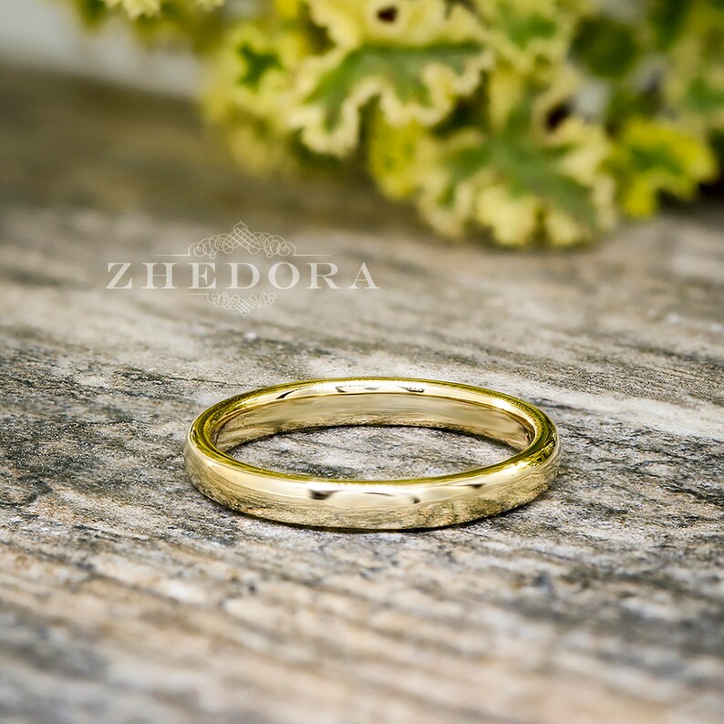 May include: A simple gold wedding band with a polished finish. The band is shown on a wooden surface.
