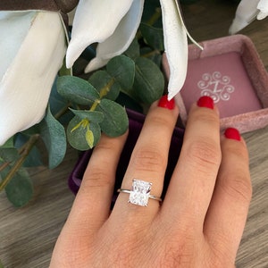 May include: A silver ring with a large, clear, rectangular-shaped diamond. The ring is on a finger with red nail polish.