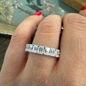 May include: A white gold eternity band featuring a row of emerald-cut diamonds.