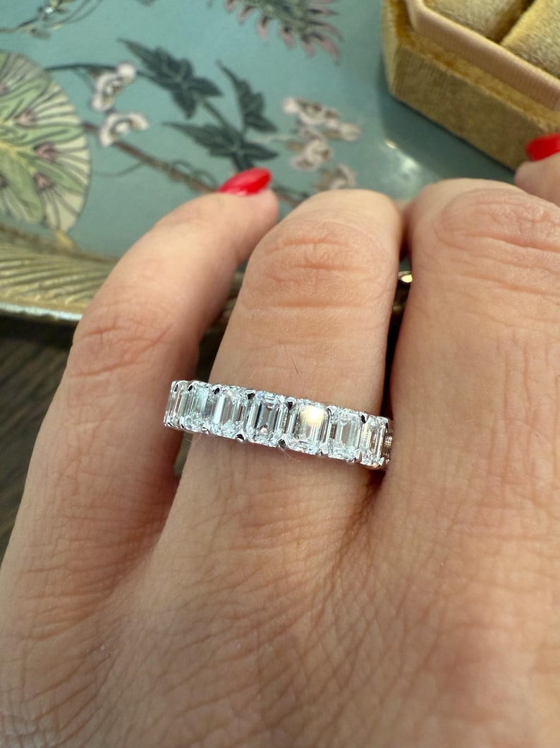 May include: A white gold eternity band featuring a row of emerald-cut diamonds.