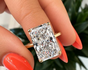 Puede incluir: Un anillo con una piedra preciosa transparente de corte radiante montada en una banda de oro amarillo pulido. La gran piedra rectangular presenta múltiples facetas que reflejan la luz, asegurada por cuatro garras de oro en las esquinas.