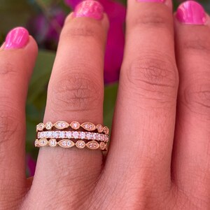 May include: Three gold rings with a delicate design featuring small, round diamonds and oval-shaped accents. The rings are stacked on a finger.