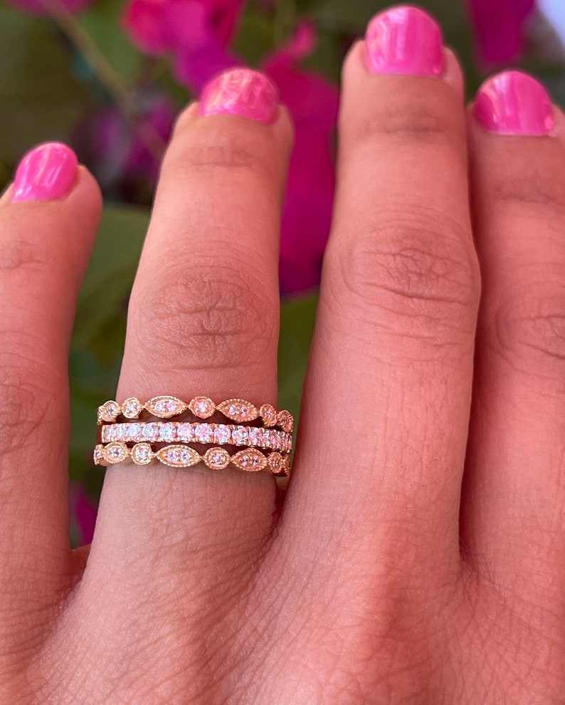 May include: Three gold rings with a delicate design featuring small, round diamonds and oval-shaped accents. The rings are stacked on a finger.