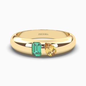 May include: A gold band ring with a green emerald and a yellow pear-shaped gemstone. The ring is engraved with the word "ZHEDORA".