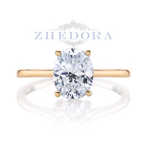 Puede incluir: Un anillo de compromiso de oro con un diamante de forma ovalada. El anillo est&aacute; engastado en una banda fina.