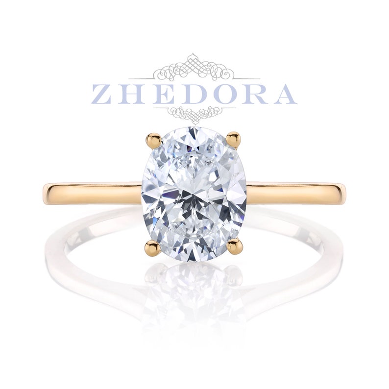 Puede incluir: Un anillo de compromiso de oro con un diamante de forma ovalada. El anillo est&aacute; engastado en una banda fina.