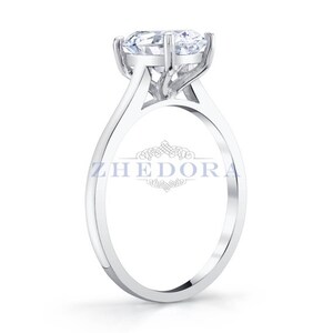 Puede incluir: Un anillo de compromiso solitario de plata con un gran diamante redondo y claro engastado en un engaste de cuatro garras. La banda es fina y tiene un acabado pulido.