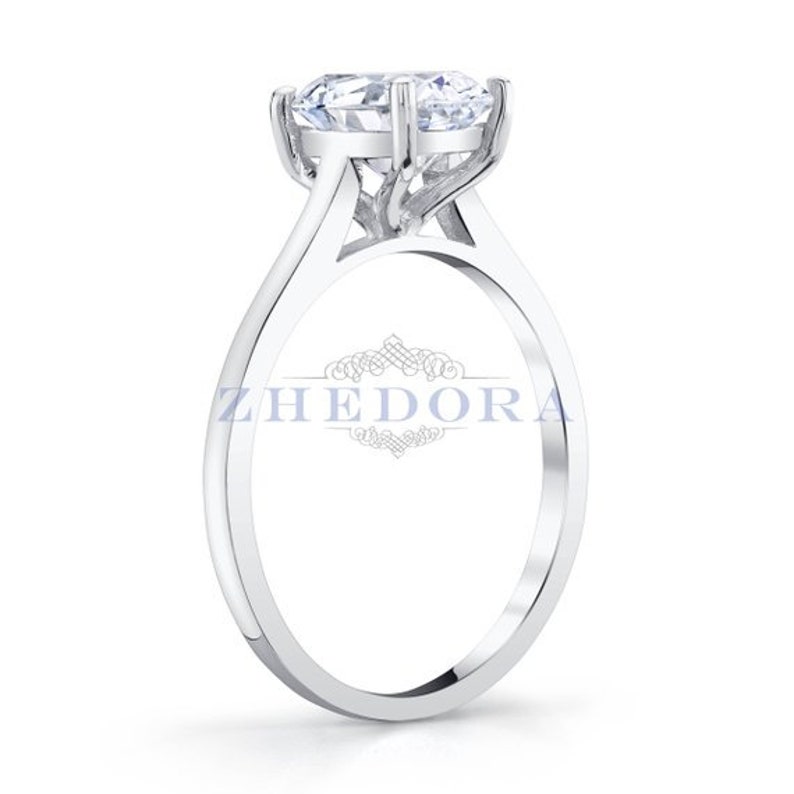 Puede incluir: Un anillo de compromiso solitario de plata con un gran diamante redondo y claro engastado en un engaste de cuatro garras. La banda es fina y tiene un acabado pulido.
