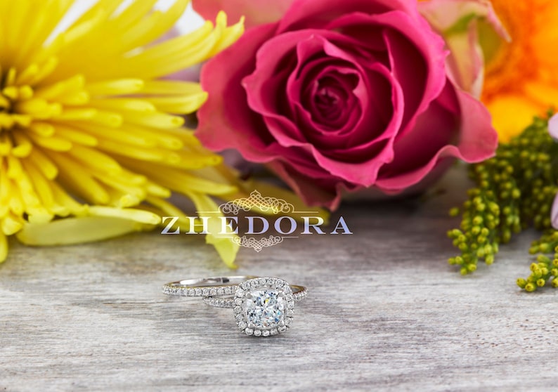 May include: A silver engagement ring set with a square-cut diamond surrounded by smaller diamonds. The ring is on a wooden surface with yellow, pink, and orange flowers.