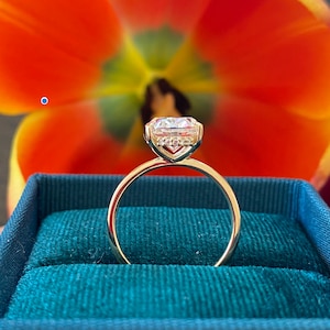 May include: A gold engagement ring with a large, clear, round diamond in a prong setting. The ring is in a green velvet ring box.