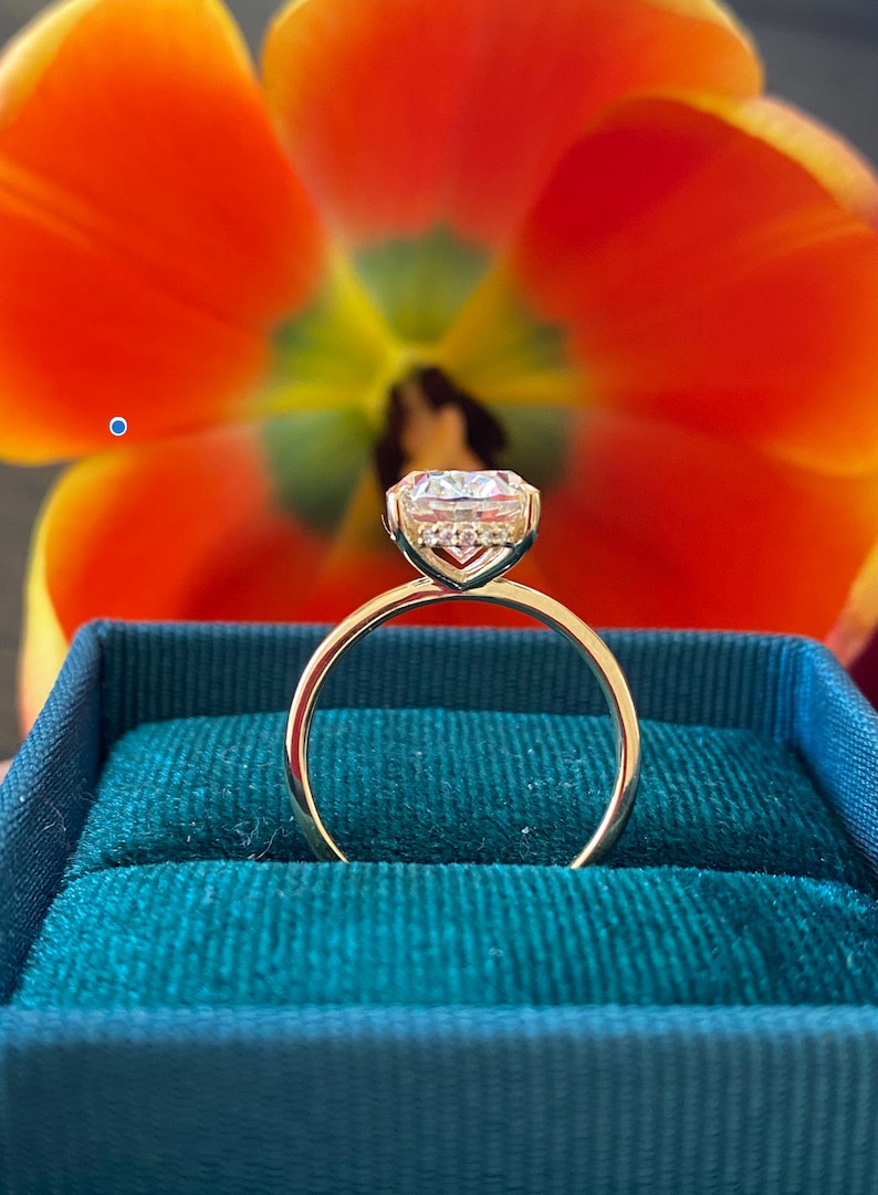 May include: A gold engagement ring with a large, clear, round diamond in a prong setting. The ring is in a green velvet ring box.