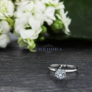 May include: A silver solitaire engagement ring with a round brilliant cut diamond. The ring is set on a simple band and features a six-prong setting.