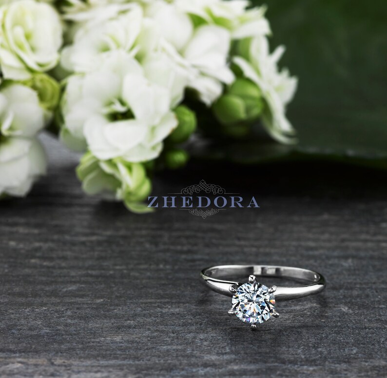 May include: A silver solitaire engagement ring with a round brilliant cut diamond. The ring is set on a simple band and features a six-prong setting.