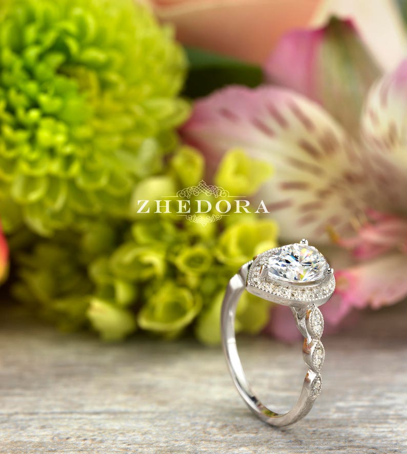 May include: A pear-shaped diamond engagement ring with a halo setting and a delicate, twisted band. The ring is set in silver and features a row of small diamonds on the band.