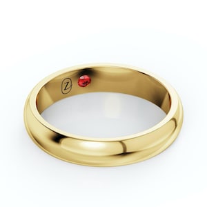 May include: A gold ring with a polished finish. The ring has a small, round, red gemstone and a stylized letter "Z" engraved on the band. The ring is set against a white background.