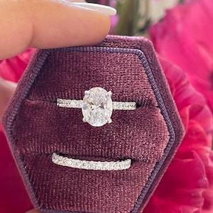 May include: A close-up of a silver ring set with a large oval-shaped diamond. The ring is in a burgundy velvet ring box.