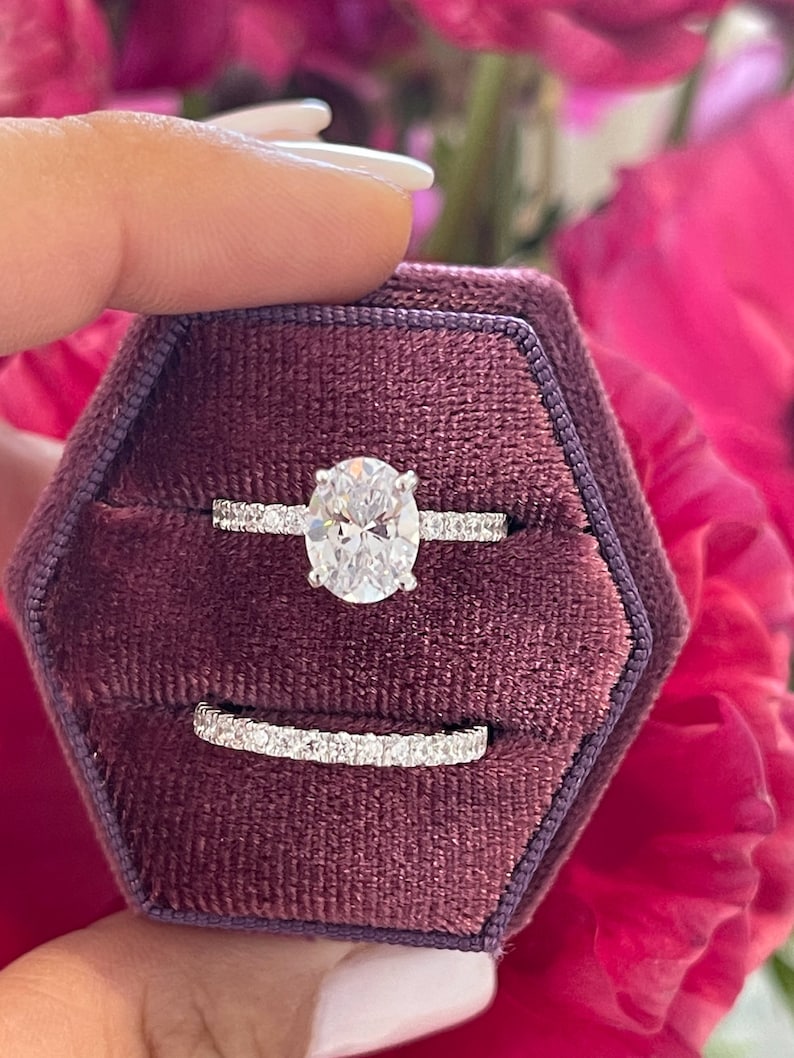 May include: A close-up of a silver ring set with a large oval-shaped diamond. The ring is in a burgundy velvet ring box.