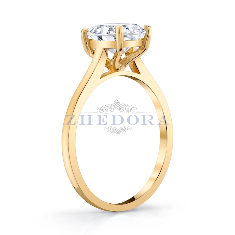Puede incluir: Un anillo de compromiso de oro con un gran diamante redondo y claro engastado en una garra de cuatro puntas. El anillo tiene una banda simple.