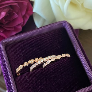 May include: Two delicate rose gold rings with a row of small diamonds set in a leaf pattern. The rings are displayed in a purple velvet ring box.