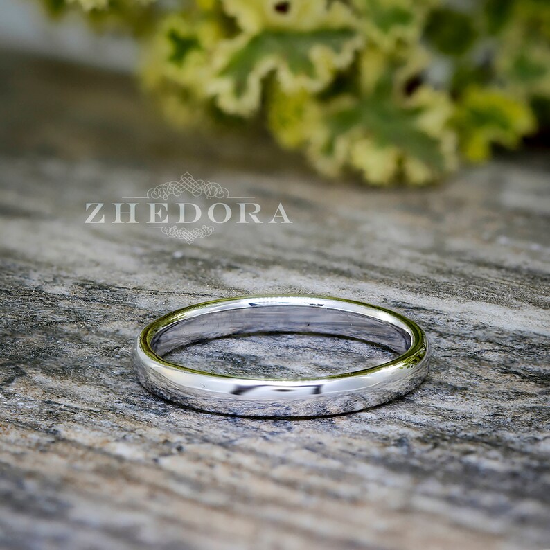 May include: A simple, polished silver wedding band. The band is smooth and has a slightly rounded edge.