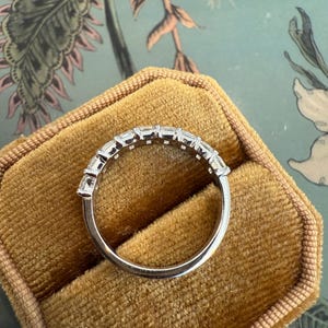 May include: A silver band with a row of small, clear, rectangular-shaped stones set in a continuous line around the band.