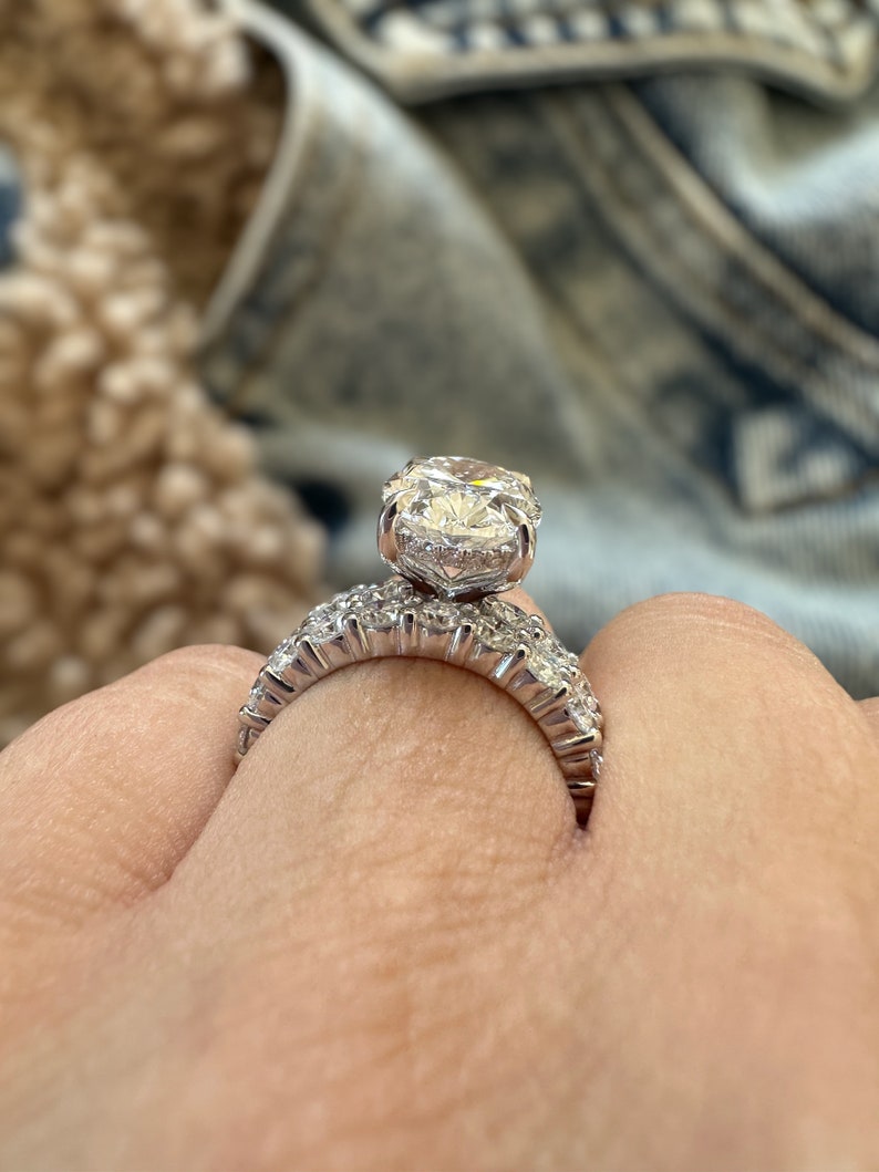 K&ouml;nnte beinhalten: Nahaufnahme eines Diamant-Verlobungsrings. Der Ring hat einen gro&szlig;en, rund geschliffenen Diamanten als Mittelstein, der von einem Halo aus kleineren Diamanten umgeben ist. Das Band ist ebenfalls mit Diamanten besetzt, was einen funkelnden Effekt erzeugt. Der Ring ist aus Silbermetall.