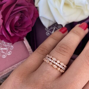May include: Three delicate rose gold rings with a pave setting of small round diamonds. The rings are stacked on a finger and feature a leaf-like design.