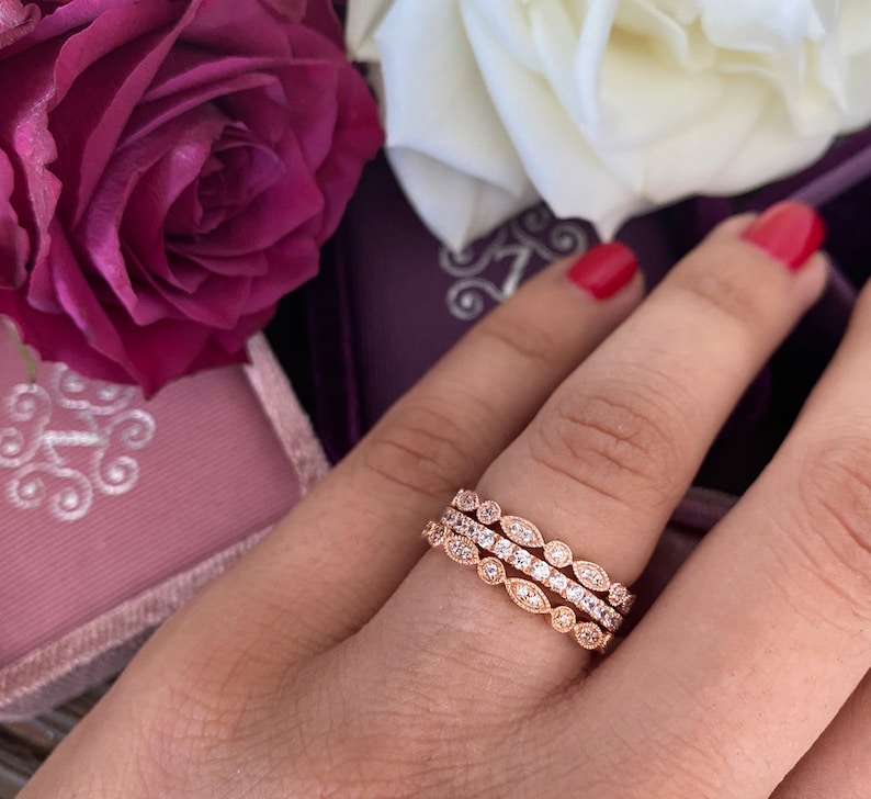 May include: Three delicate rose gold rings with a pave setting of small round diamonds. The rings are stacked on a finger and feature a leaf-like design.