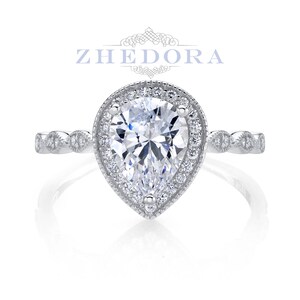 May include: A pear-shaped diamond engagement ring with a halo setting and a delicate, twisted band. The ring is set in silver and features a sparkling, clear diamond.