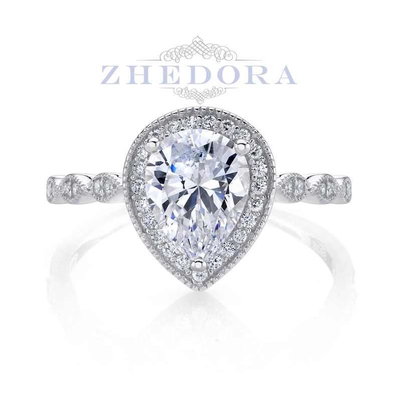 May include: A pear-shaped diamond engagement ring with a halo setting and a delicate, twisted band. The ring is set in silver and features a sparkling, clear diamond.