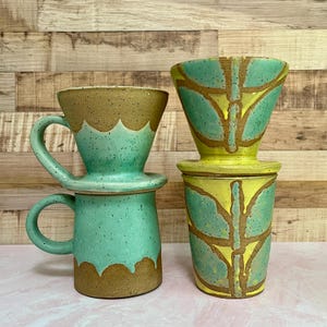 May include: Two ceramic coffee pour-over sets. One set is turquoise with a brown rim and handle. The other set is yellow and green with a brown leaf design. Both sets are handmade and have a rustic aesthetic.