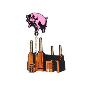 Op de afbeelding: Een roze varken dat boven een zwart en oranje gebouw vliegt met een zilveren ketting die ze verbindt. Het gebouw heeft hoge schoorstenen en is een weergave van de Battersea Power Station.