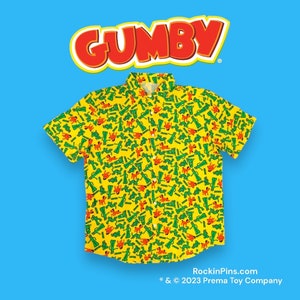 May include: A yellow short-sleeved button-down shirt with a pattern of green and orange Gumby figures. The shirt has a collar and a pocket on the left side. The text "GUMBY" is in red letters at the top of the image. The text "RockinPins.com * & © 2023 Prema Toy Company" is at the bottom of the image.