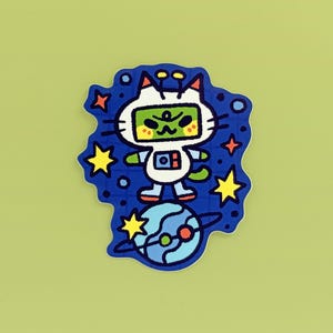 May include: A sticker featuring a cartoon cat in a space suit, standing on a planet. The cat is white with a green face and is surrounded by stars and planets on a blue background. The sticker has a light green background.