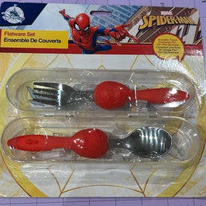May include: A Marvel Spider-Man flatware set in a clear plastic package. The set includes a fork and spoon with red handles and a Spider-Man design. The packaging has the Disney logo and the words "Flatware Set" and "Ensemble De Couverts".
