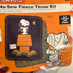 May include: A Peanuts No-Sew Fleece Throw Kit with Snoopy dressed as a vampire and a mummy. The kit includes a purple and green fleece throw with a Halloween theme. The throw measures 72in x 60in (182.9cm x 152.4cm).