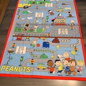 May include: A Peanuts-themed playmat with a red border and a blue background. The playmat features a winding road with various characters from the Peanuts comic strip, including Snoopy, Charlie Brown, Lucy, and Linus. The road is lined with trees, houses, and other objects. The playmat also includes a number of math problems, such as 3+5, 2+6, 9-1, and 10-2. The playmat is made of a soft, durable material and is perfect for children of all ages.