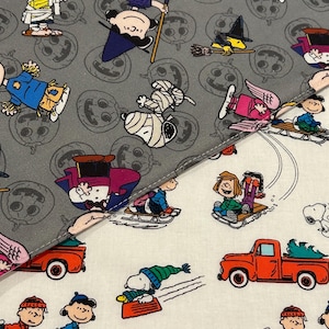 May include: Fabric featuring a repeating pattern of cartoon characters in Halloween and winter scenes. The top half is gray with jack-o'-lanterns and characters in costumes. The bottom half is white with sledding and red truck designs.